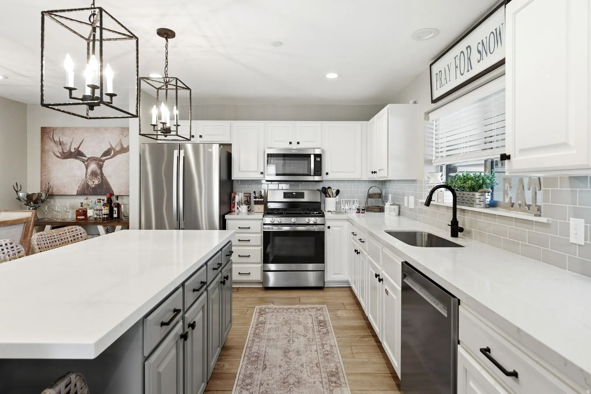 Two tone kitchen featuring dual tone cabinetry, stainless steel appliances, light stone countertops, light wood-style flooring, and backsplash