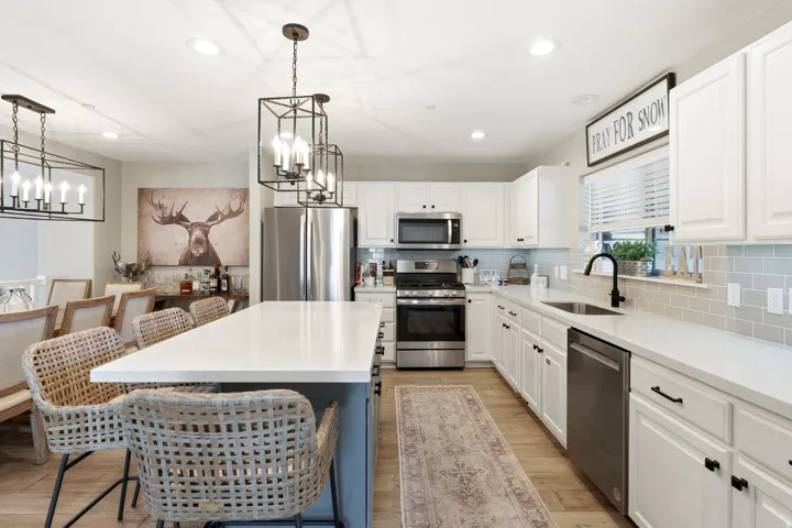 Kitchen featuring stainless steel appliances, a kitchen breakfast bar, a center island, two tone color scheme, and suspended lighting