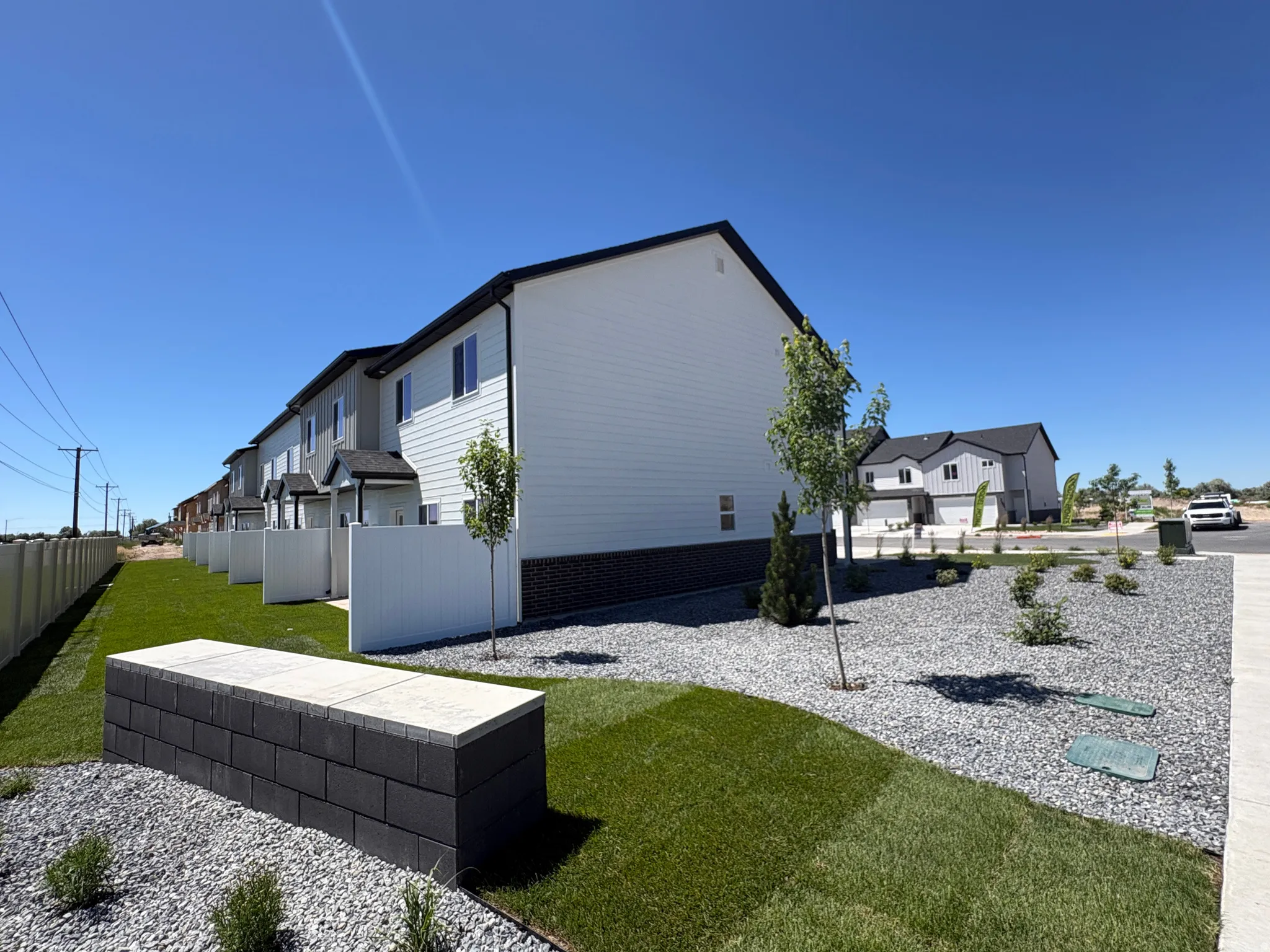 Contemporary row of properties featuring white siding with dark trim, individual fenced patio areas, and a well-maintained lawn