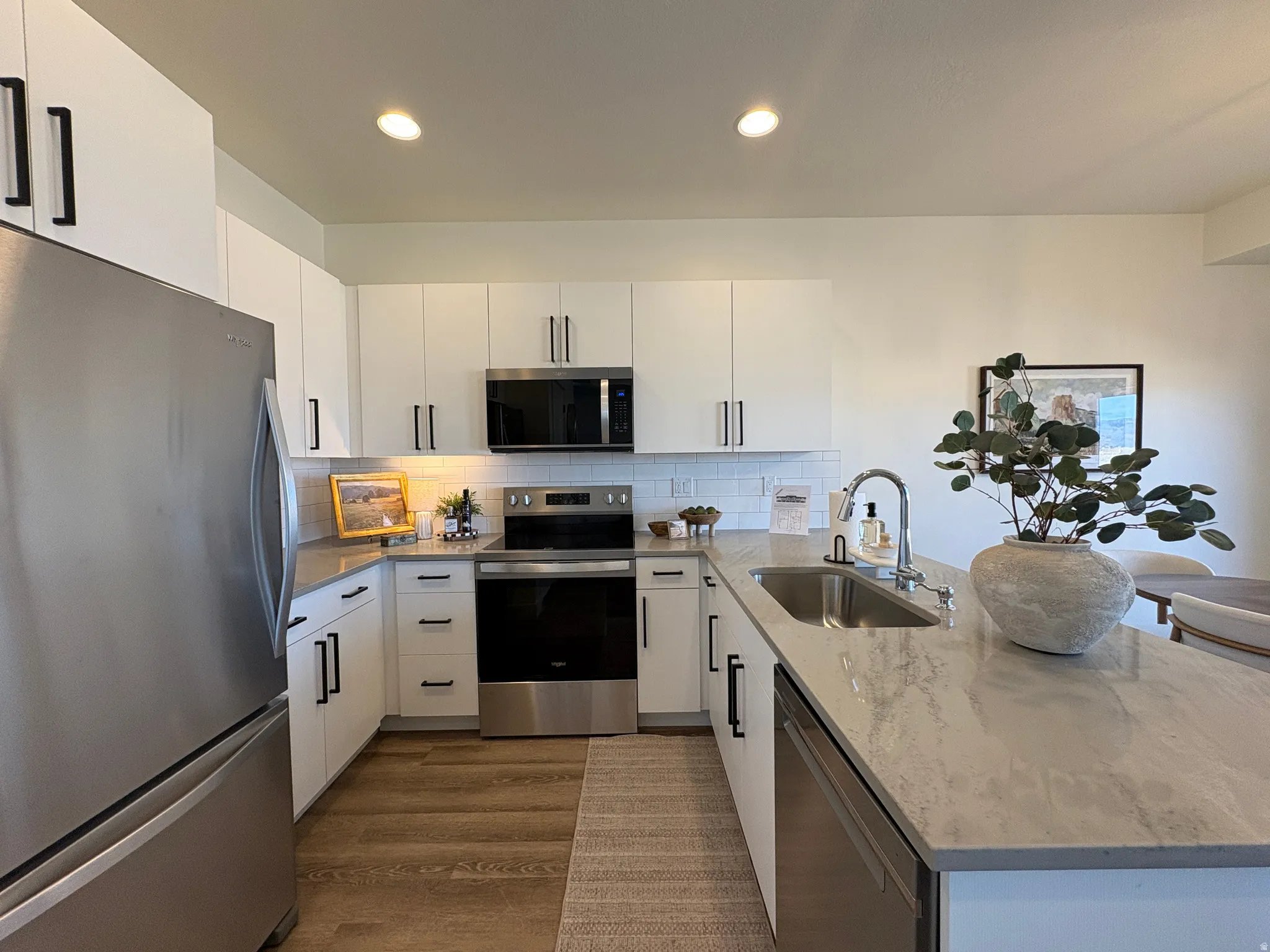 Kitchen with stainless steel appliances, a peninsula, white cabinetry, light stone countertops, and recessed lighting