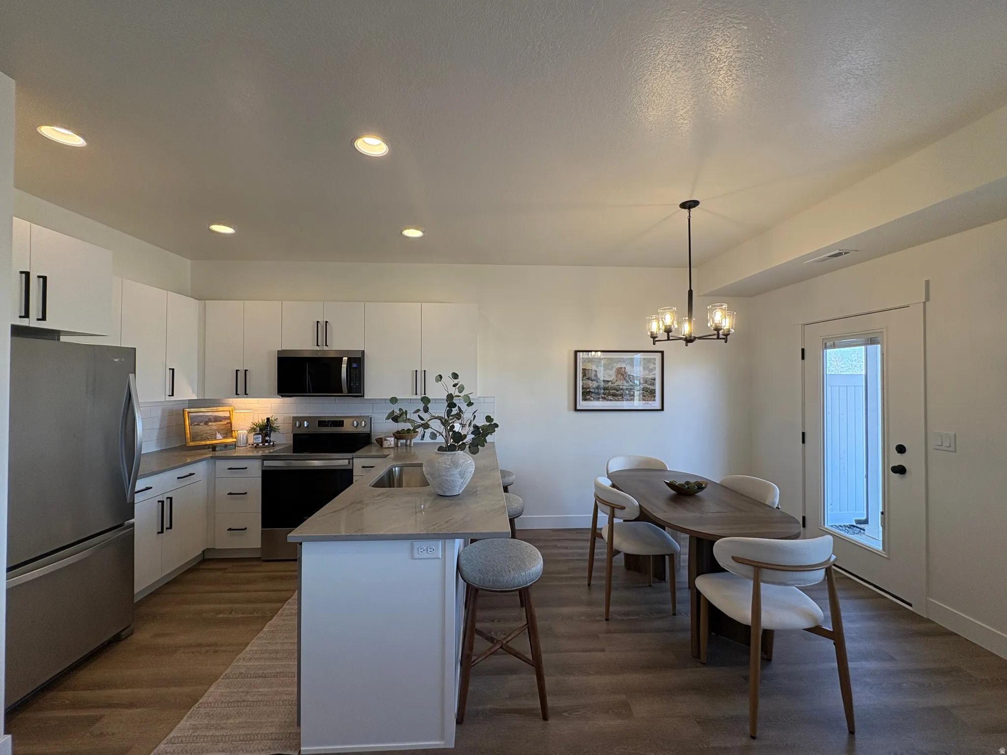 Kitchen with stainless steel appliances, white cabinets, decorative backsplash, and a kitchen bar