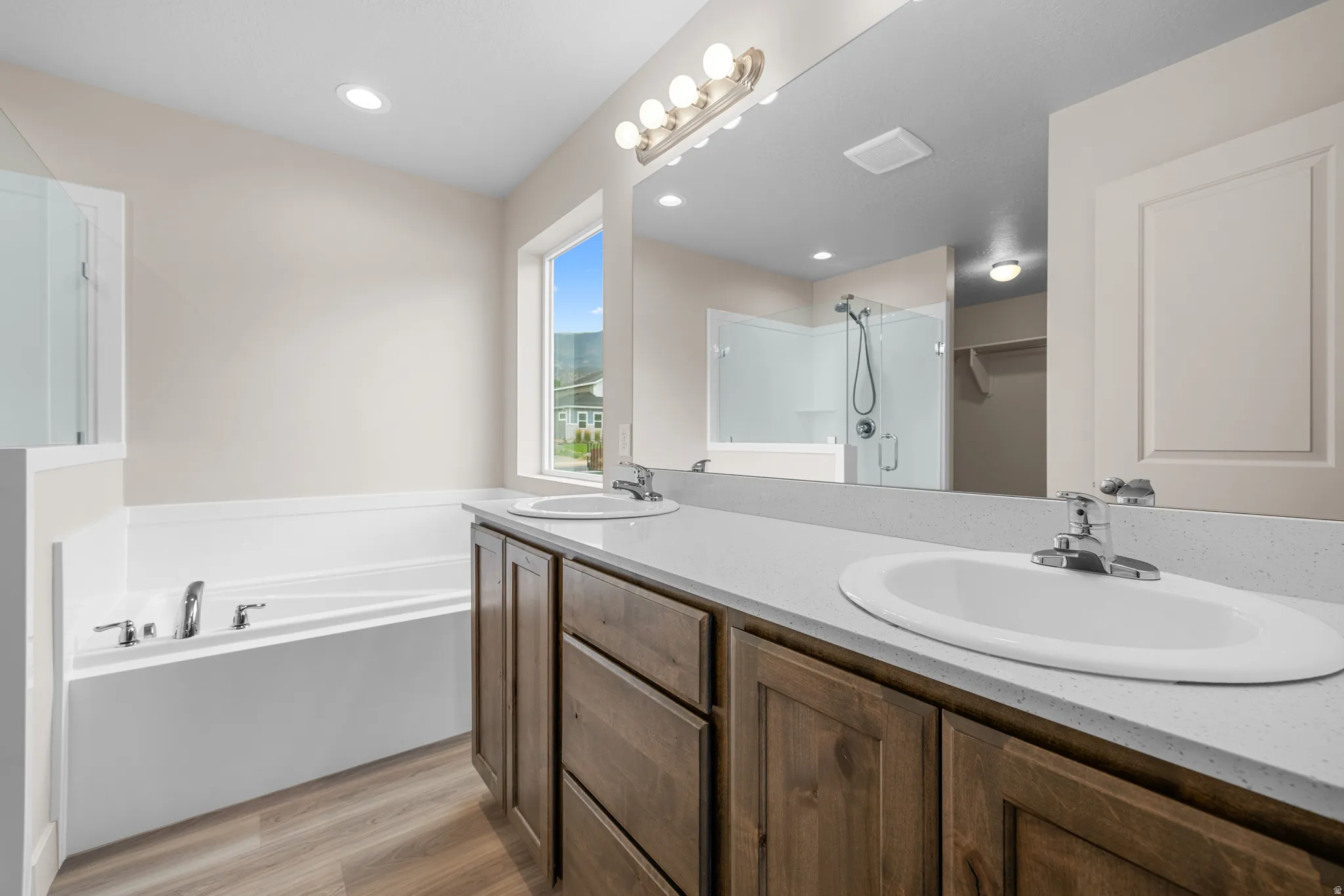 Bathroom with double vanity, a garden tub, light wood-type flooring, a shower stall, and a spacious closet