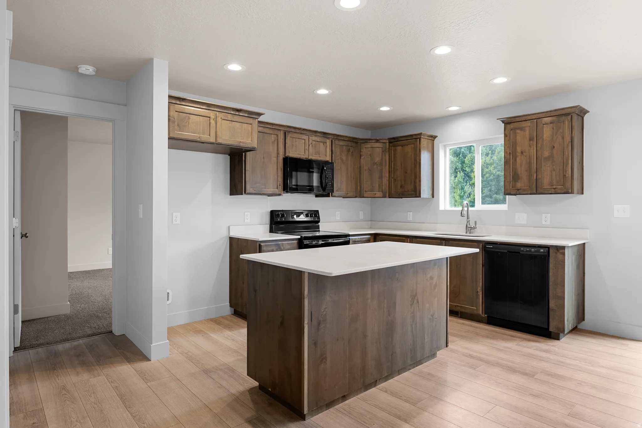 Kitchen featuring black appliances, light wood-style flooring, recessed lighting, a kitchen island, and dark wood finish cabinetry