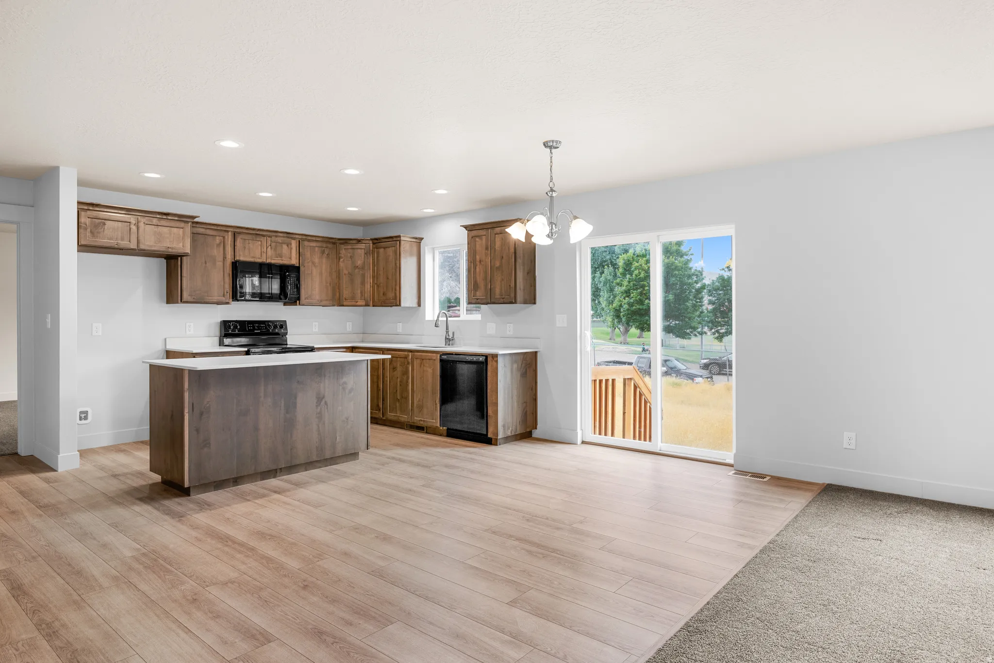 Kitchen with hanging lights, light countertops, black appliances, a kitchen island, and light wood finished floors