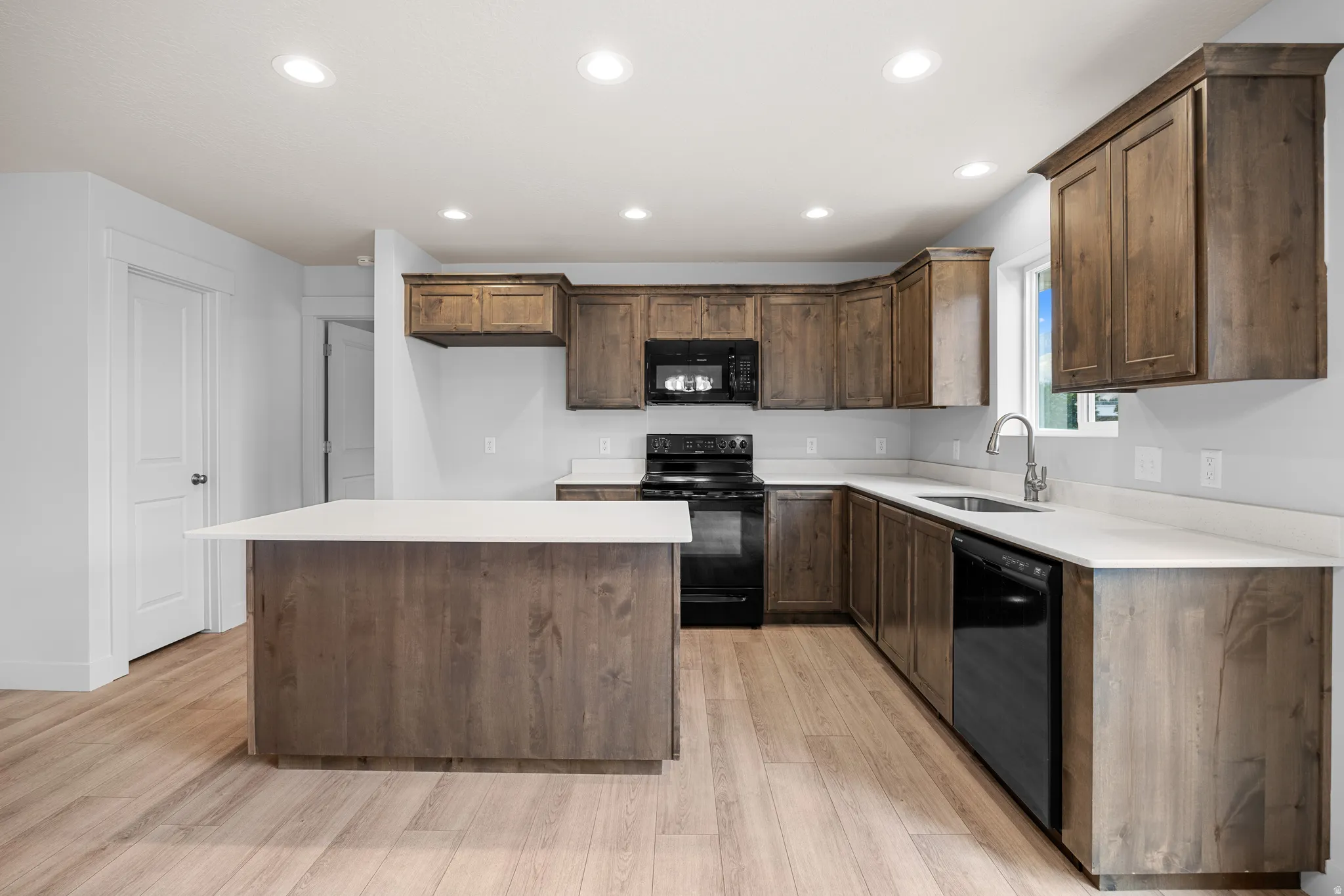 Kitchen with black appliances, a center island, recessed lighting, light wood-style floors, and dark wood finish cabinets