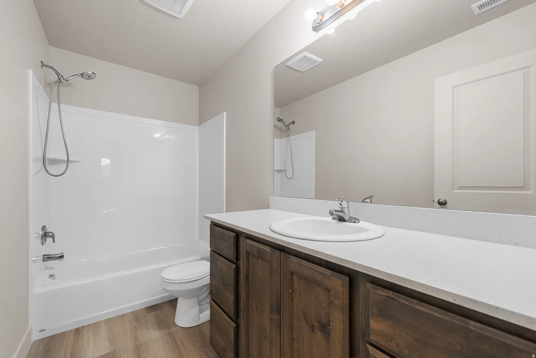 Bathroom with vanity, a textured ceiling, bathtub / shower combination, and light wood-style flooring