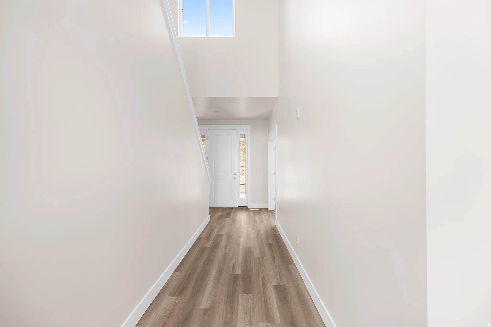 Entryway featuring wood-finish flooring, a white paneled front door with sidelight, and a high transom window