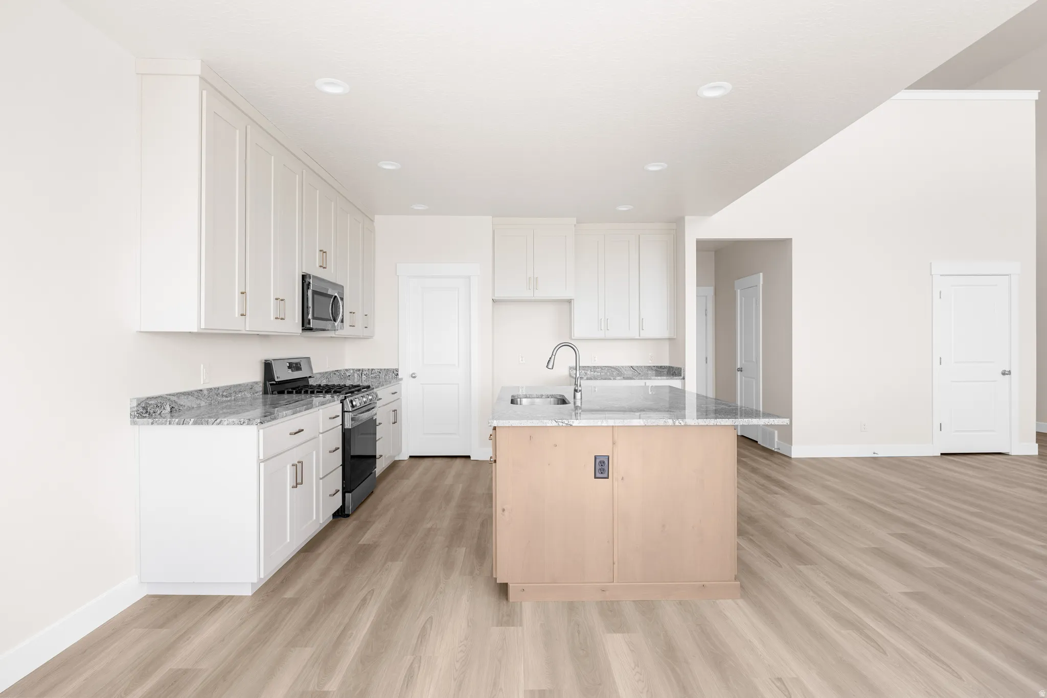 Open-concept kitchen featuring an island with an integrated sink, white cabinetry, a stainless steel microwave and range, and speckled countertops