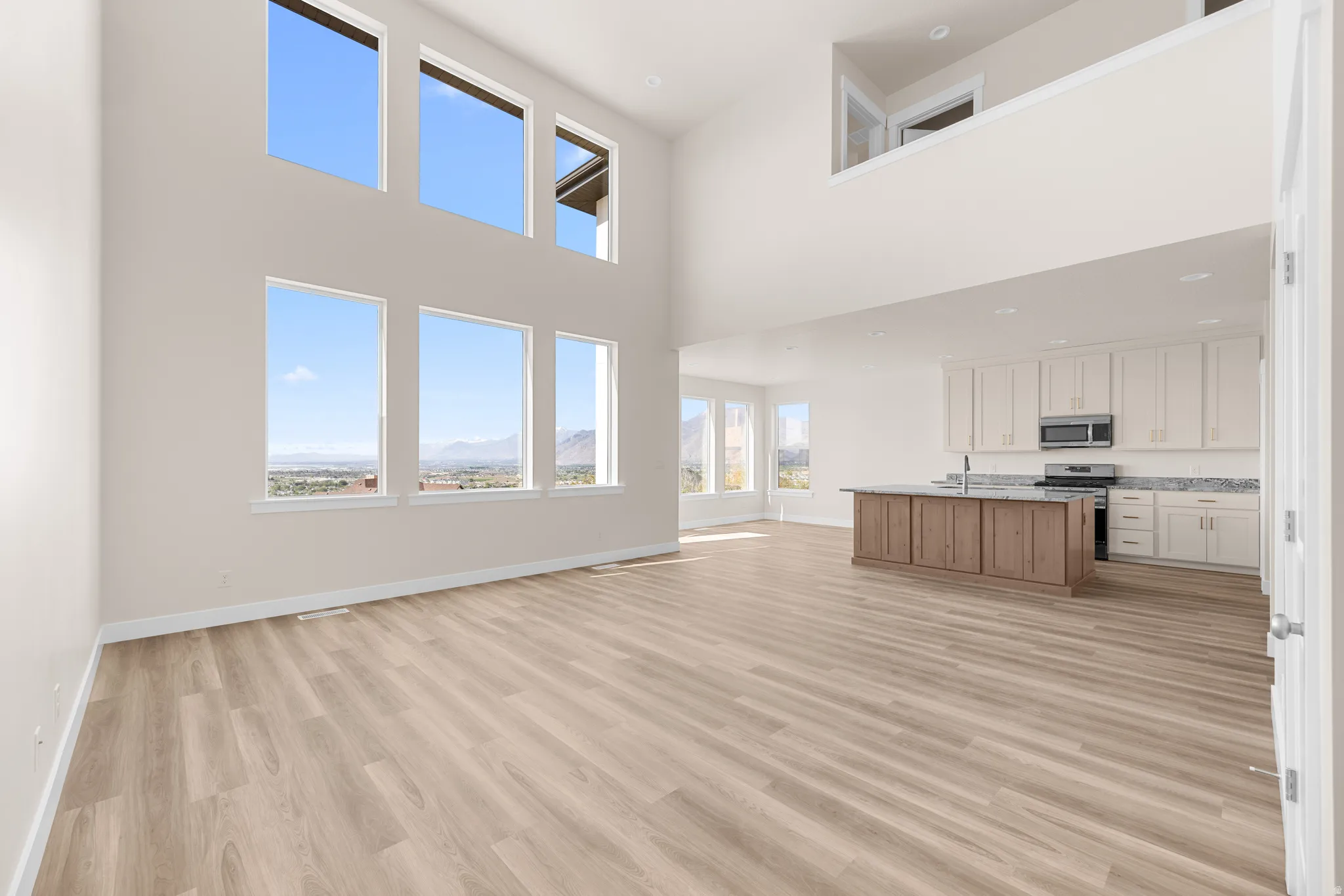 Two-story living area with high ceilings, wood-finish flooring, and a bank of six large windows