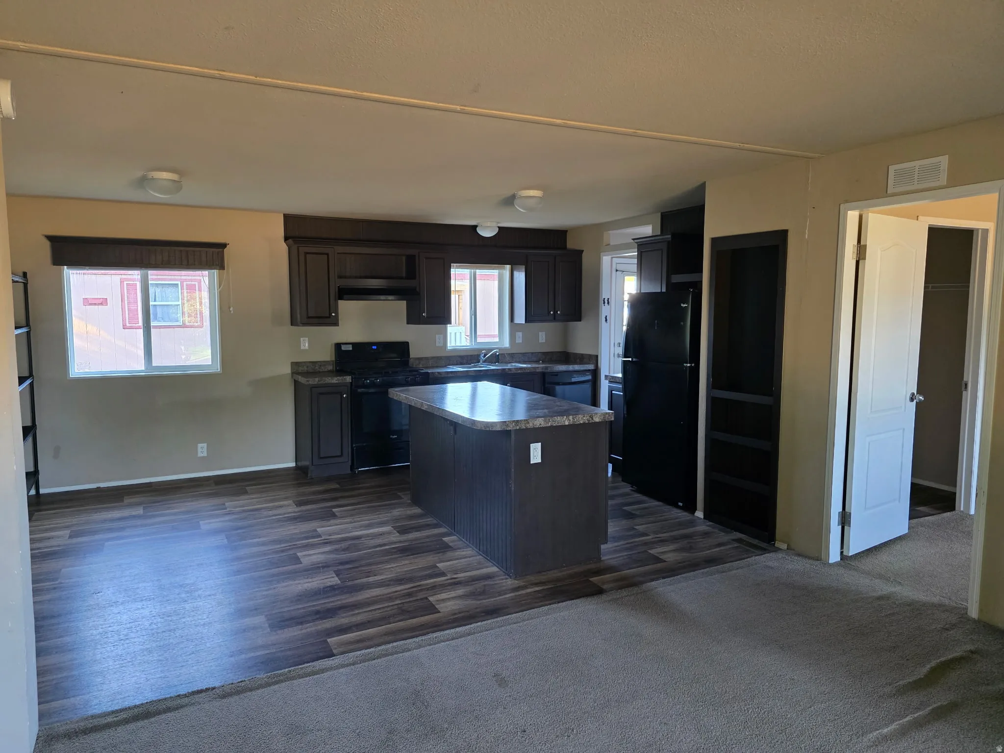 Kitchen featuring a kitchen island, black appliances, dark LVP flooring, dark wood finish cabinetry, and extractor fan