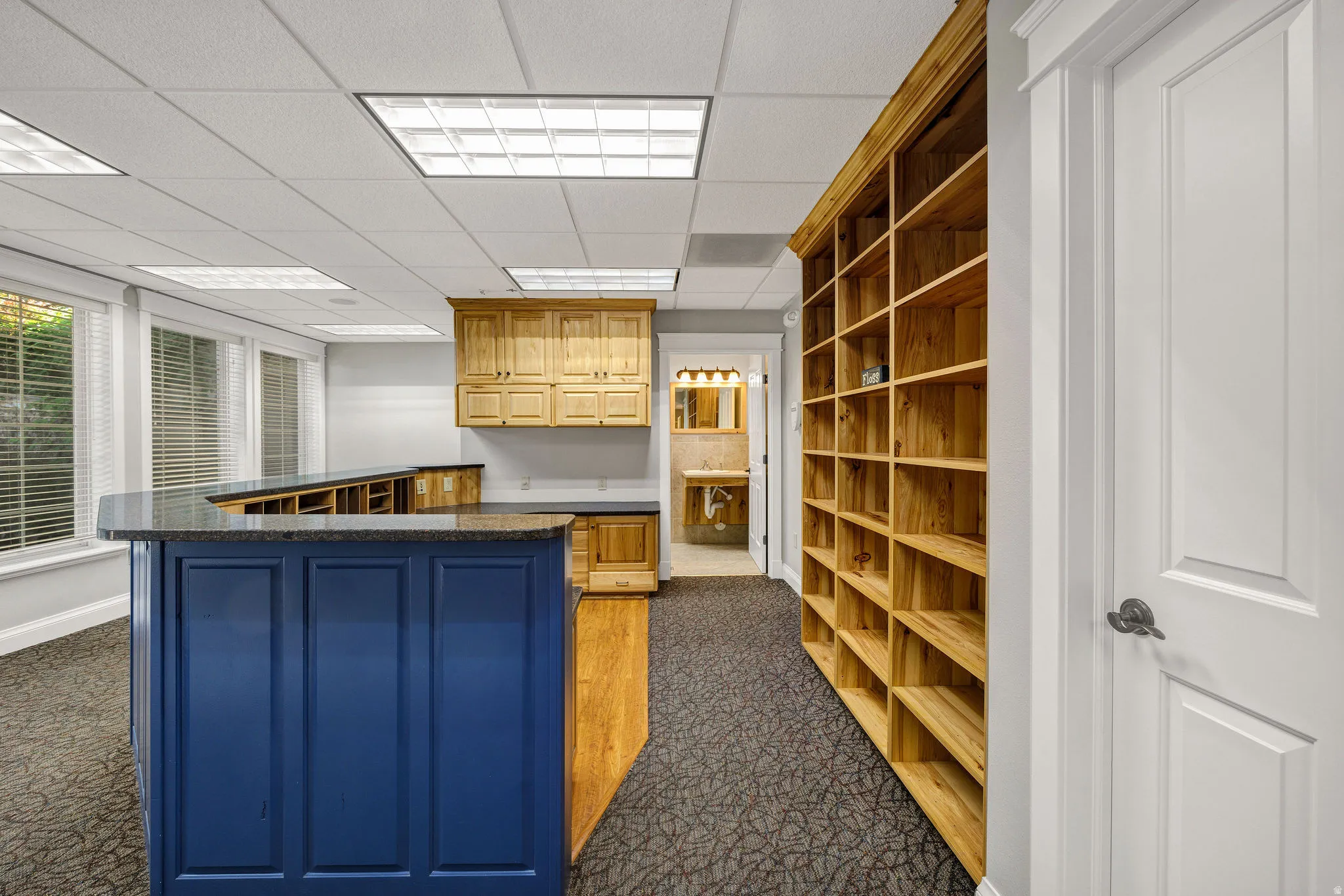 Reception area featuring dark countertops, a paneled ceiling, a reception desk, dark colored carpet, and oak cabinets