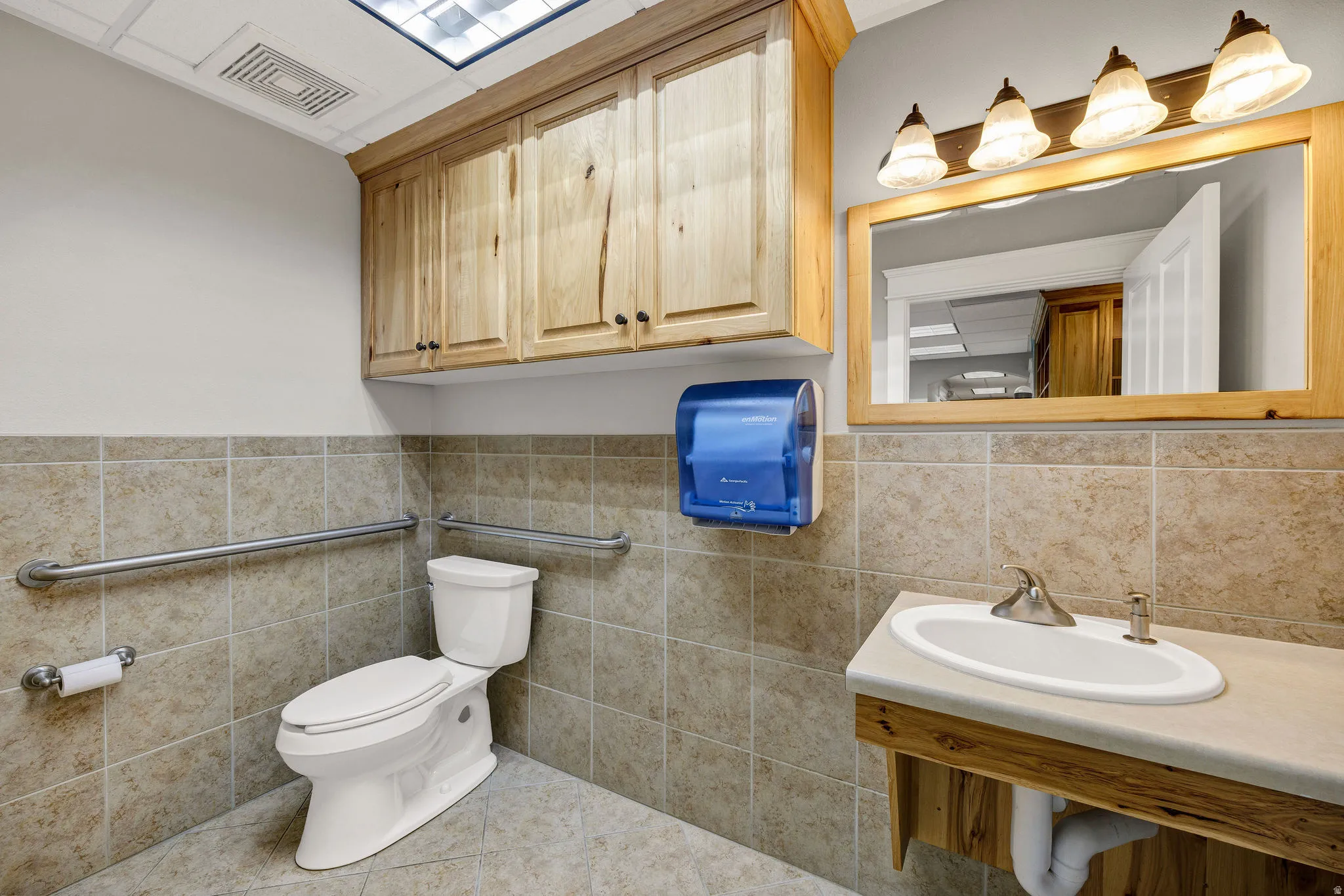 Bathroom with tile patterned flooring, a cabinet, sink, toilet and tile walls