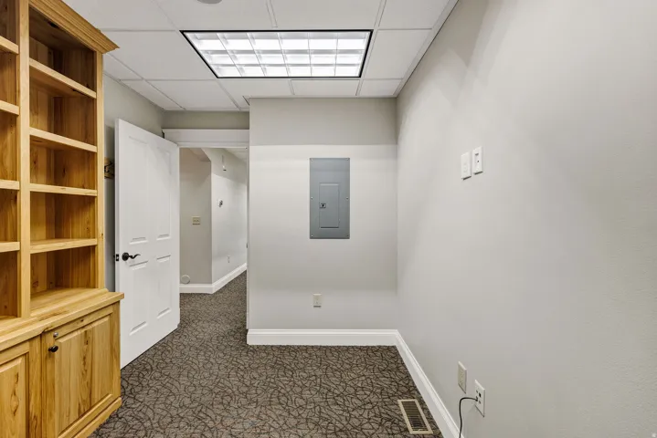 Office with dark carpet, storage cabinet, electric panel, and a drop ceiling