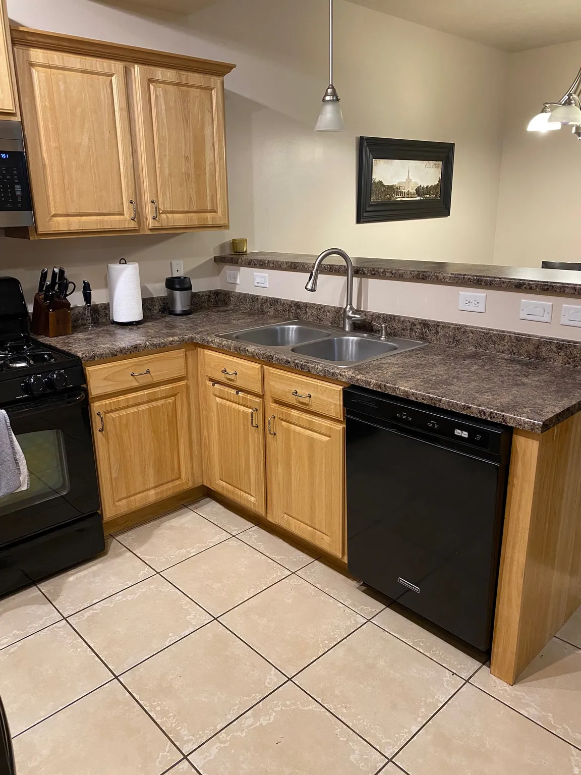 Kitchen with black appliances, dark countertops, a peninsula, hanging light fixtures, and light tile patterned flooring