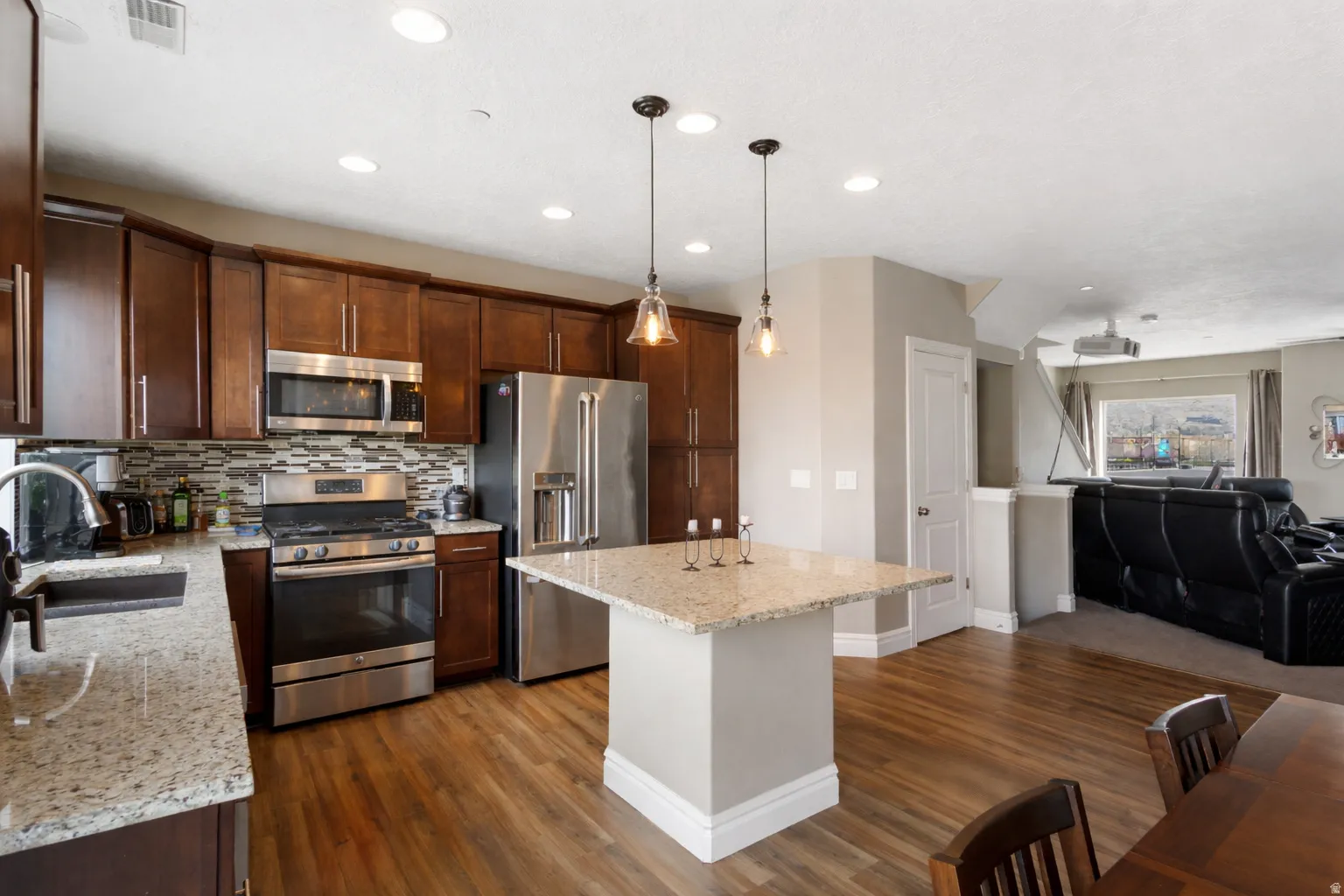 Kitchen featuring open floor plan, stainless steel appliances, light stone countertops, a kitchen island, and hanging light fixtures