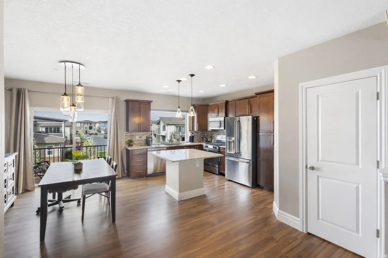 Kitchen featuring stainless steel appliances, a center island, dark wood-style floors, tasteful backsplash, and hanging light fixtures