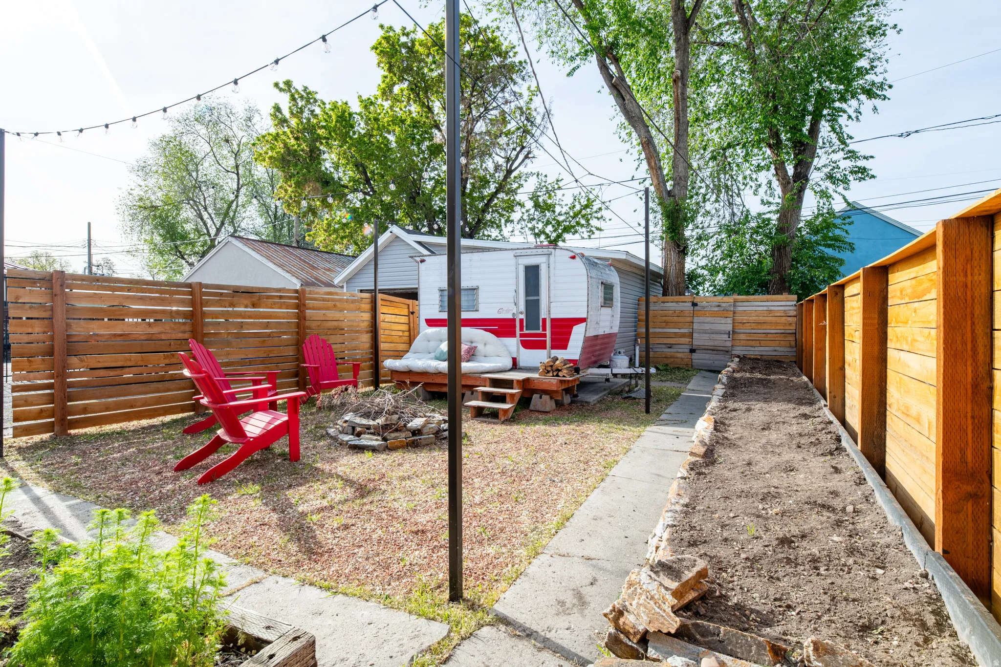 Fenced backyard featuring an outdoor fire pit, a patio, included retro camper, a detached garage, and garden beds.