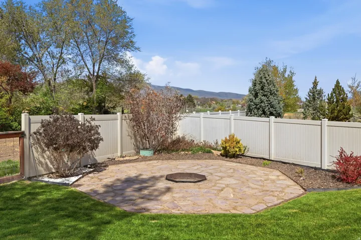 Backyard featuring a stone patio area with a fire pit, surrounded by a manicured lawn and mature shrubs