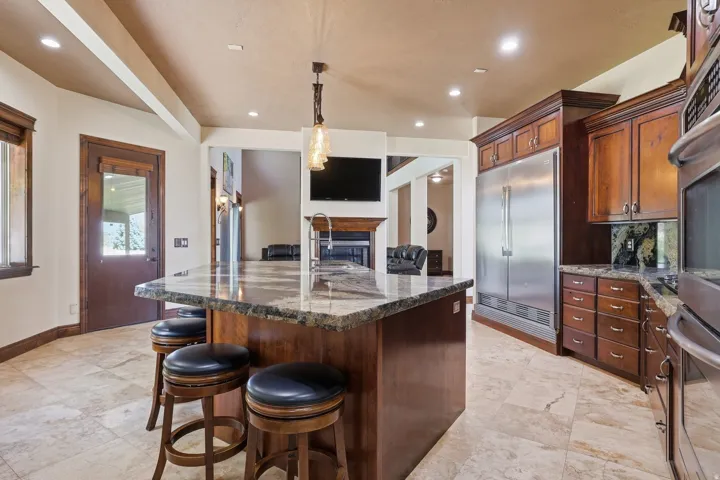 Spacious kitchen featuring a large island with stone countertop, rich wood cabinetry, stainless steel refrigerator, and built-in oven