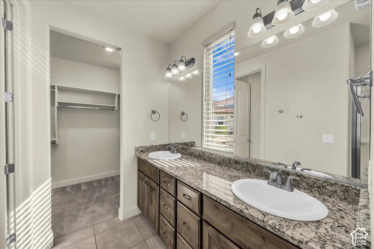 Full bath with double vanity, light tile patterned floors, and a walk in closet