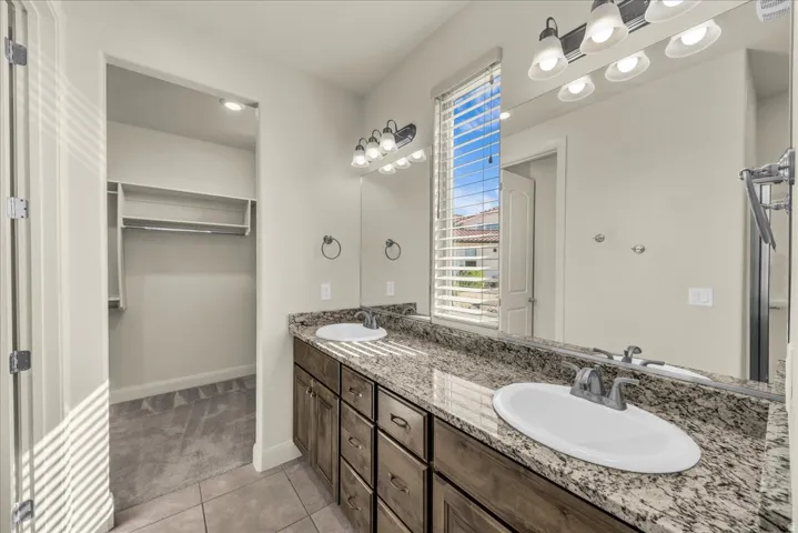 Full bath with double vanity, light tile patterned floors, and a walk in closet