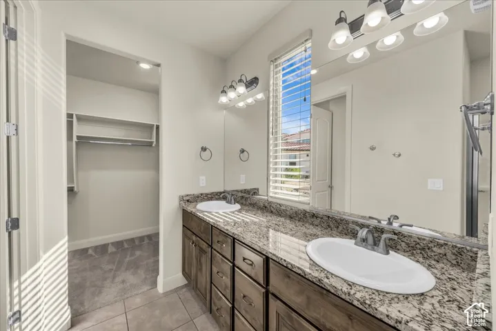 Full bath with double vanity, light tile patterned floors, and a walk in closet