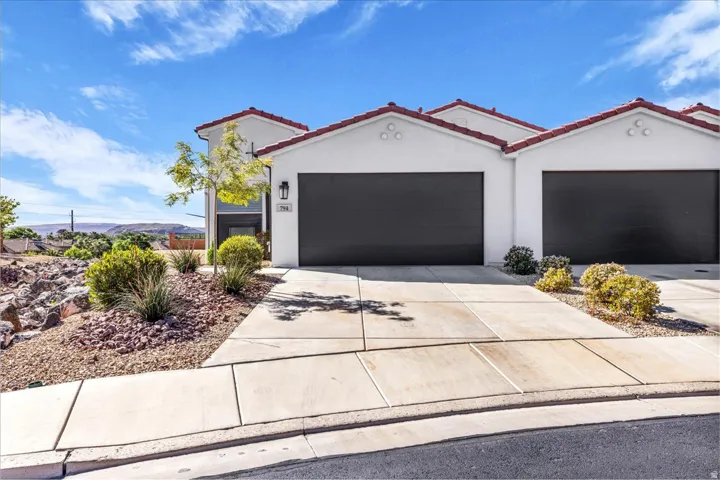 View of front facade featuring stucco siding, a tiled roof, concrete driveway, and a garage