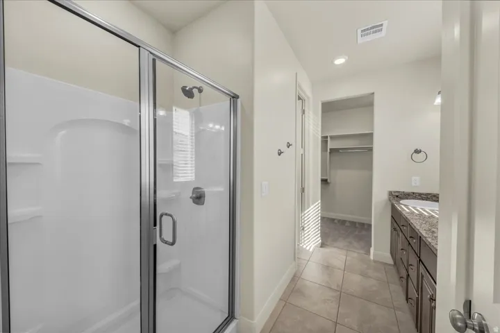 Full bath with vanity, a walk in closet, a shower stall, light tile patterned flooring, and recessed lighting