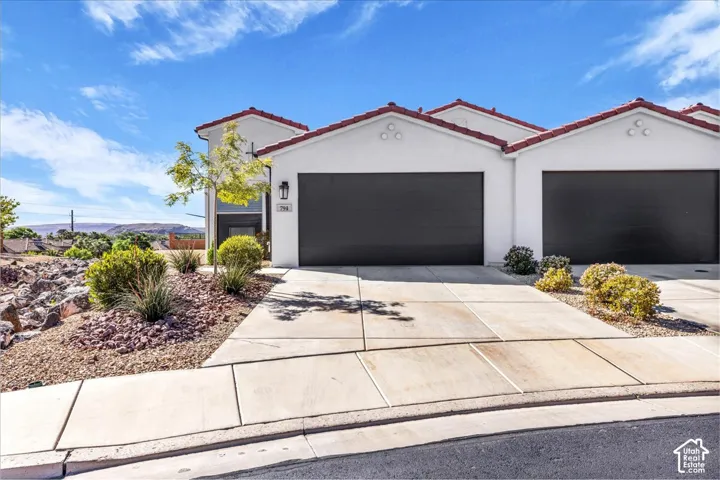 View of front facade featuring stucco siding, a tiled roof, concrete driveway, and a garage