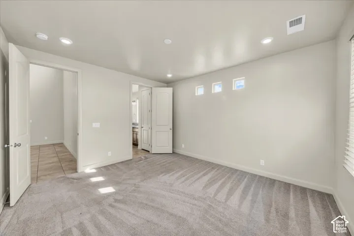 Unfurnished bedroom with light colored carpet, connected bathroom, and recessed lighting