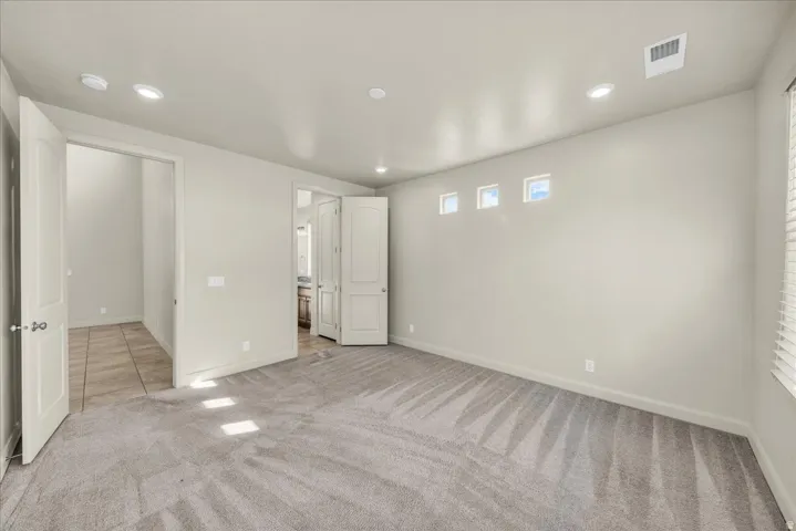 Unfurnished bedroom with light colored carpet, connected bathroom, and recessed lighting
