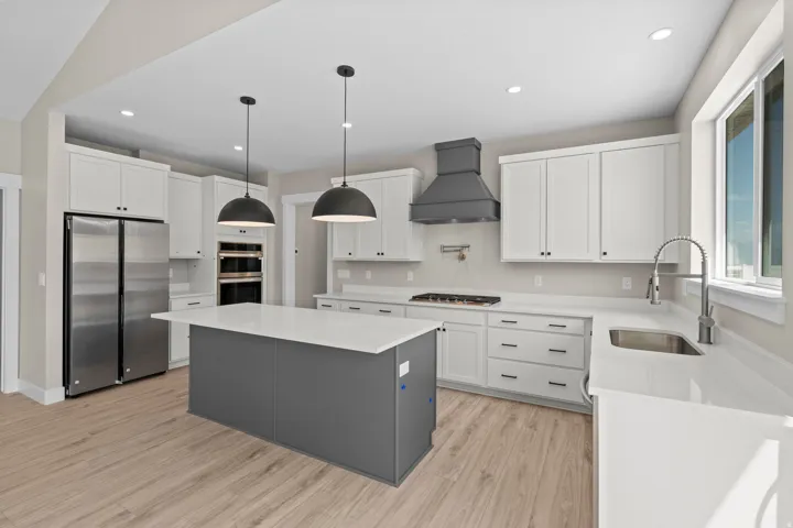 Kitchen with stainless steel appliances, light stone counters, two tone cabinets, light wood finished floors, and a center island