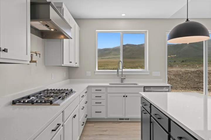 Kitchen featuring dual tone cabinets, decorative light fixtures, light stone counters, a mountain view, and stainless steel gas cooktop