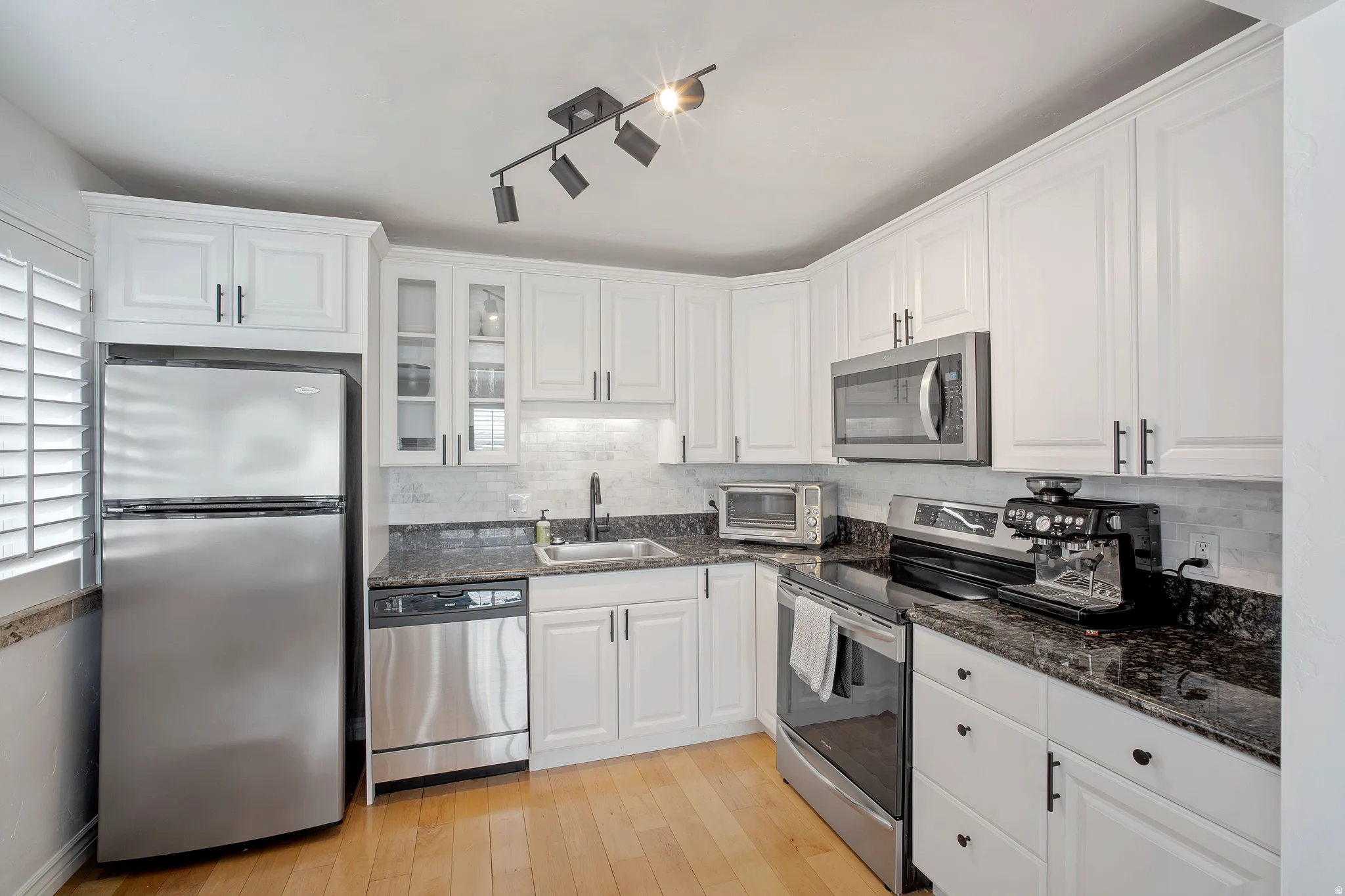 Kitchen featuring stainless steel appliances, dark stone countertops, white cabinetry, light wood-style flooring, and rail lighting