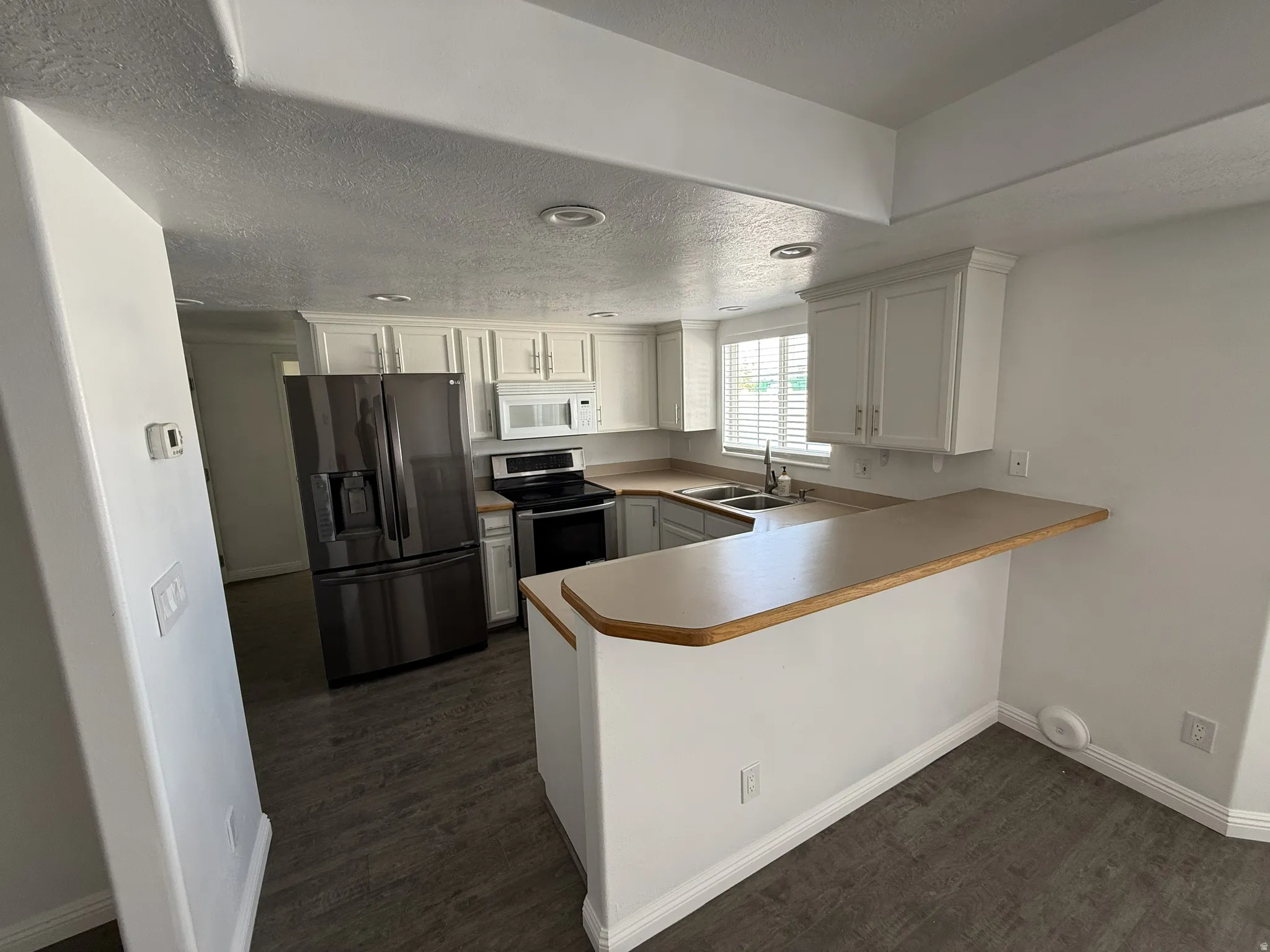 Kitchen with a peninsula, black refrigerator with ice dispenser, white cabinets, light countertops, and stainless steel range with electric stovetop