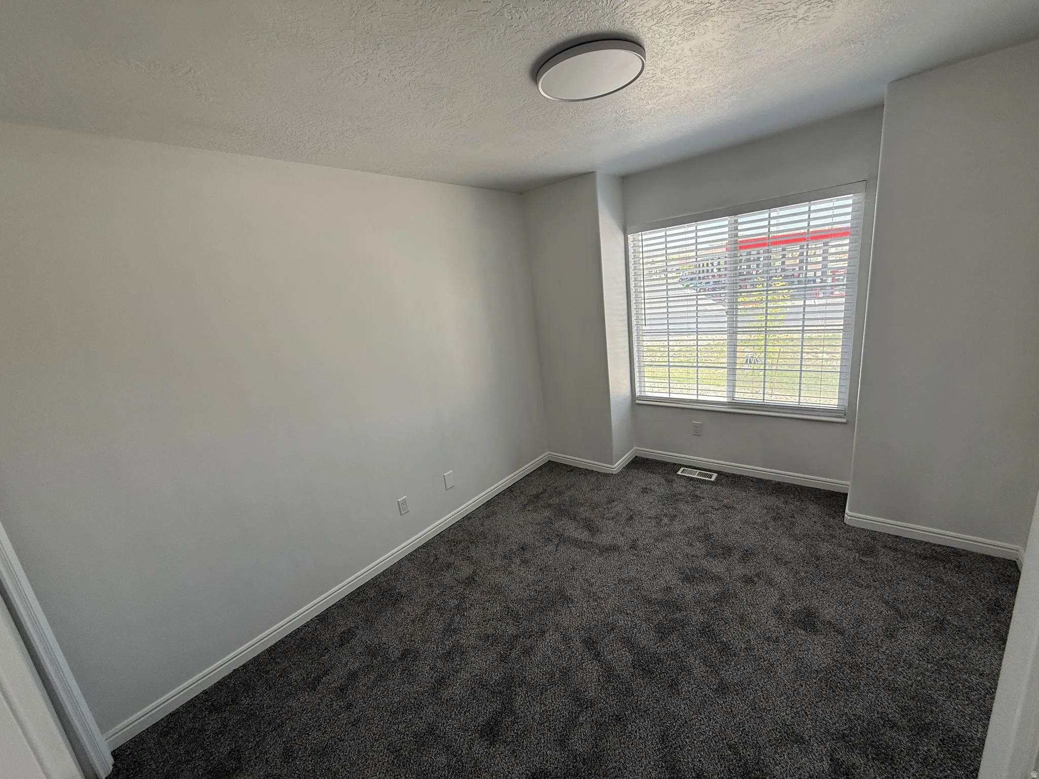 Empty room featuring dark carpet and a textured ceiling