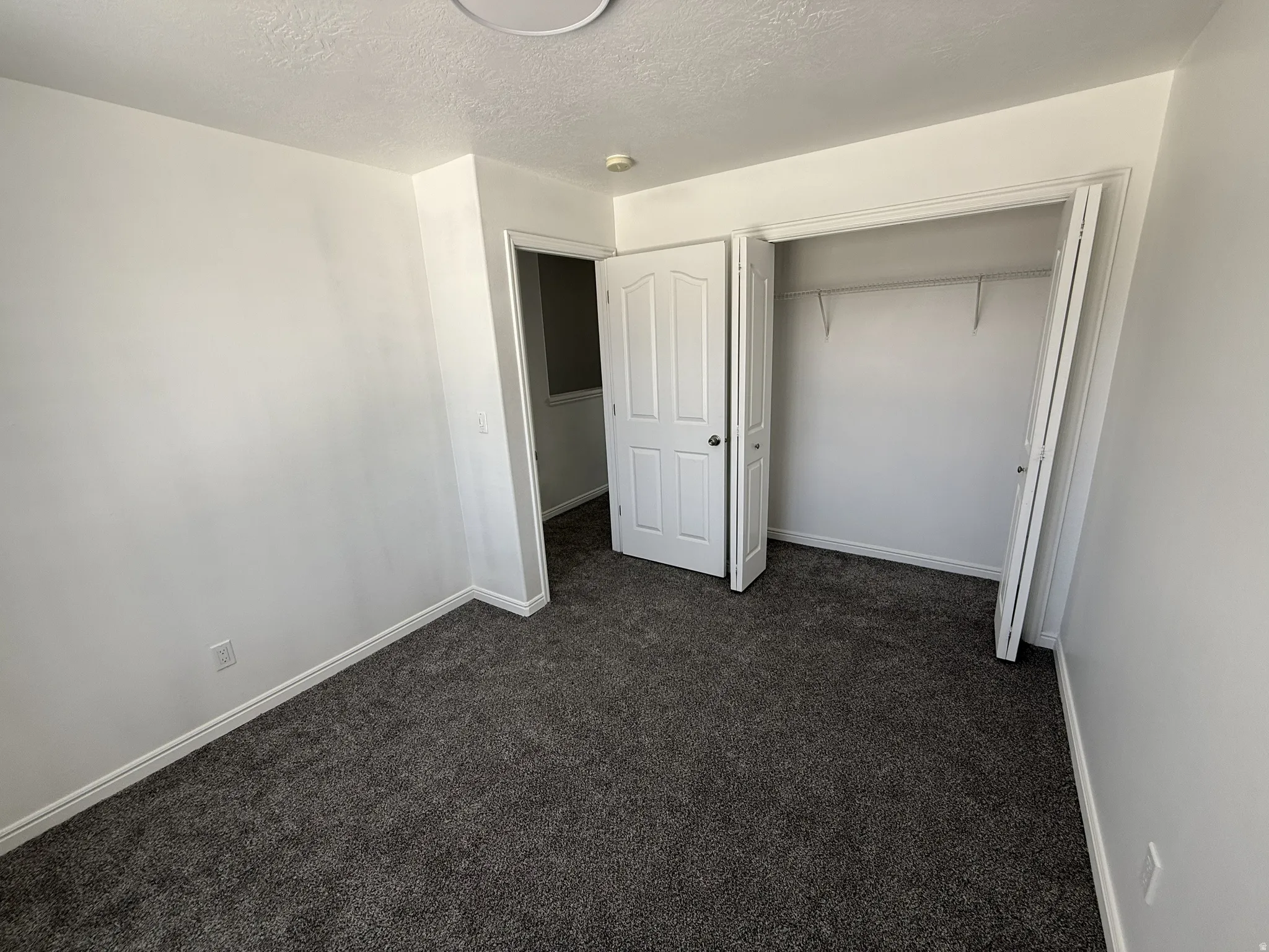 Unfurnished bedroom featuring dark colored carpet, a textured ceiling, and a closet