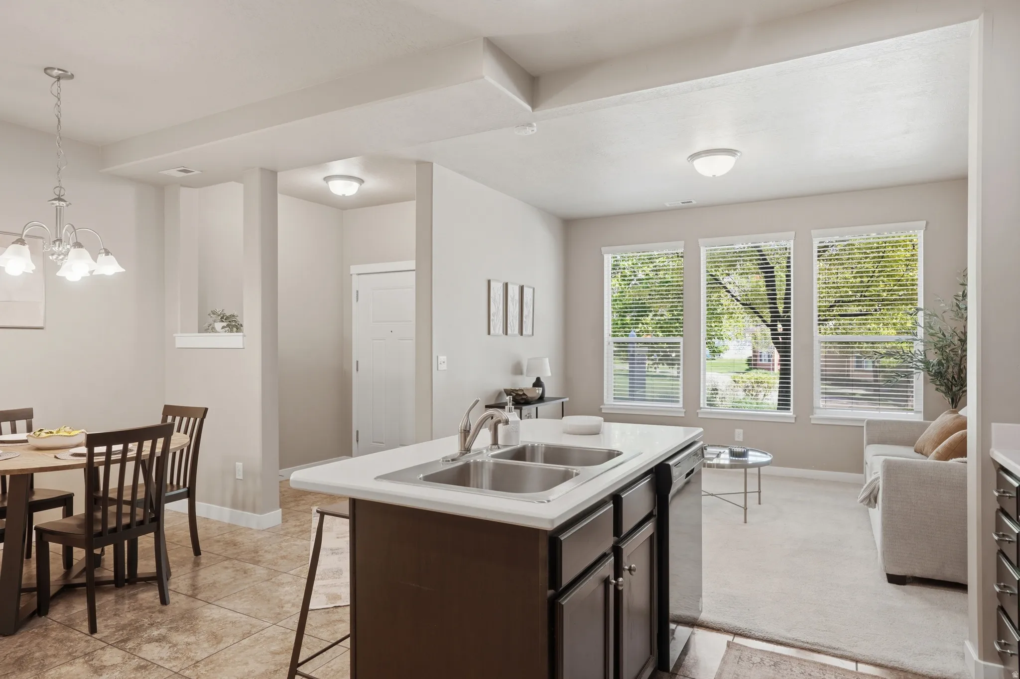 Kitchen featuring light countertops, dark wood finish cabinets, a center island with sink, dishwasher, and light carpet