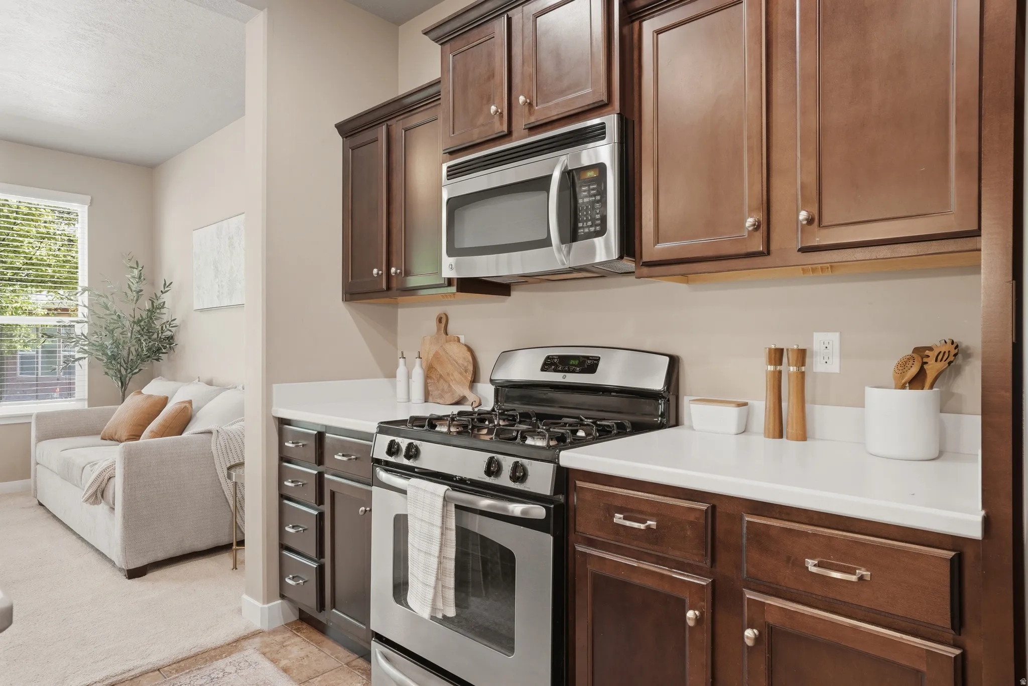 Kitchen with stainless steel appliances, light countertops, dark wood finish cabinetry, open floor plan, and light colored carpet