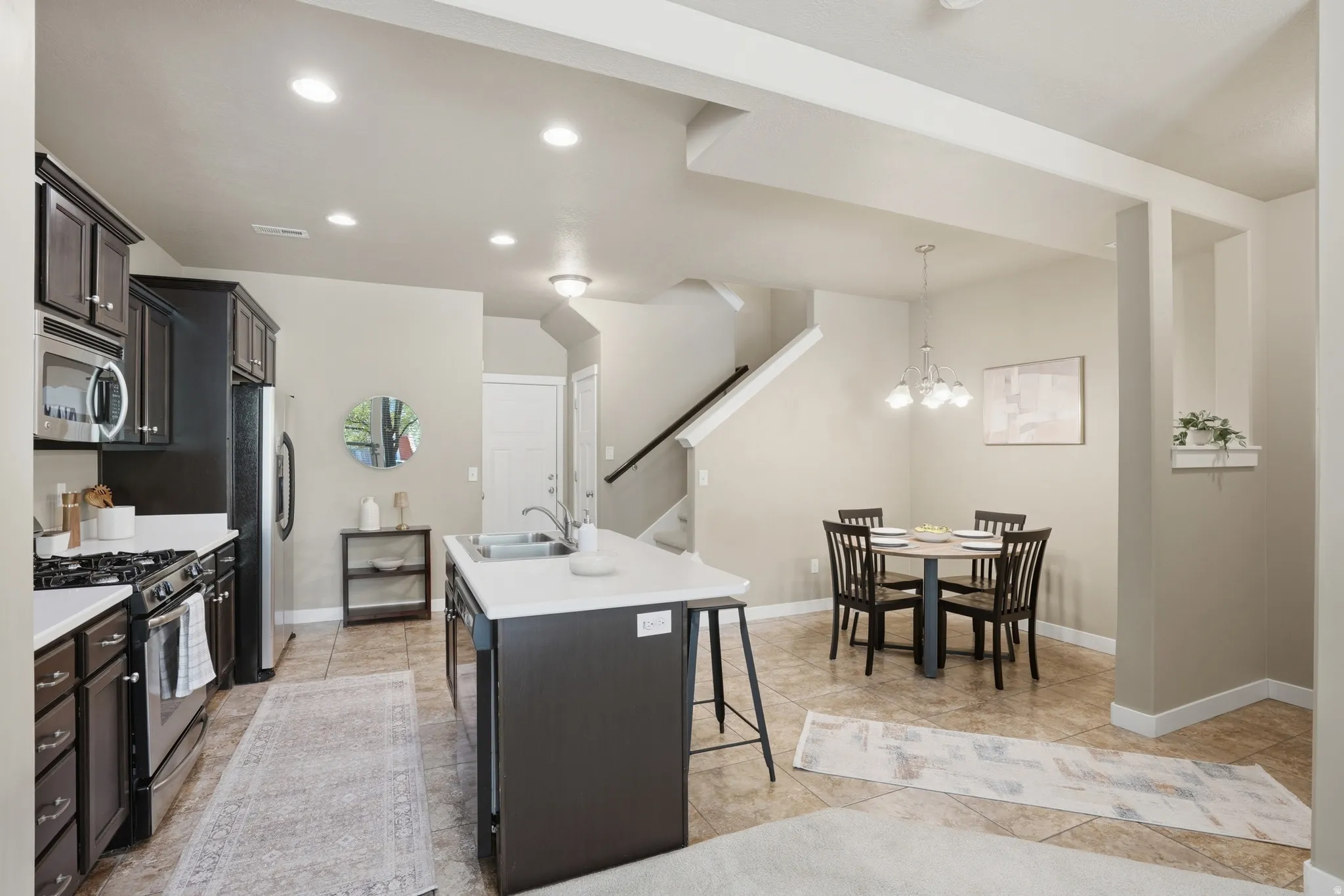 Kitchen featuring stainless steel appliances, a center island with sink, a kitchen bar, dark wood finish cabinets, and hanging lights