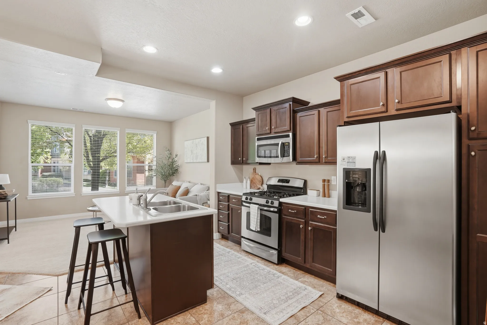 Kitchen with stainless steel appliances, light countertops, a center island with sink, a breakfast bar area, and dark wood finish cabinets