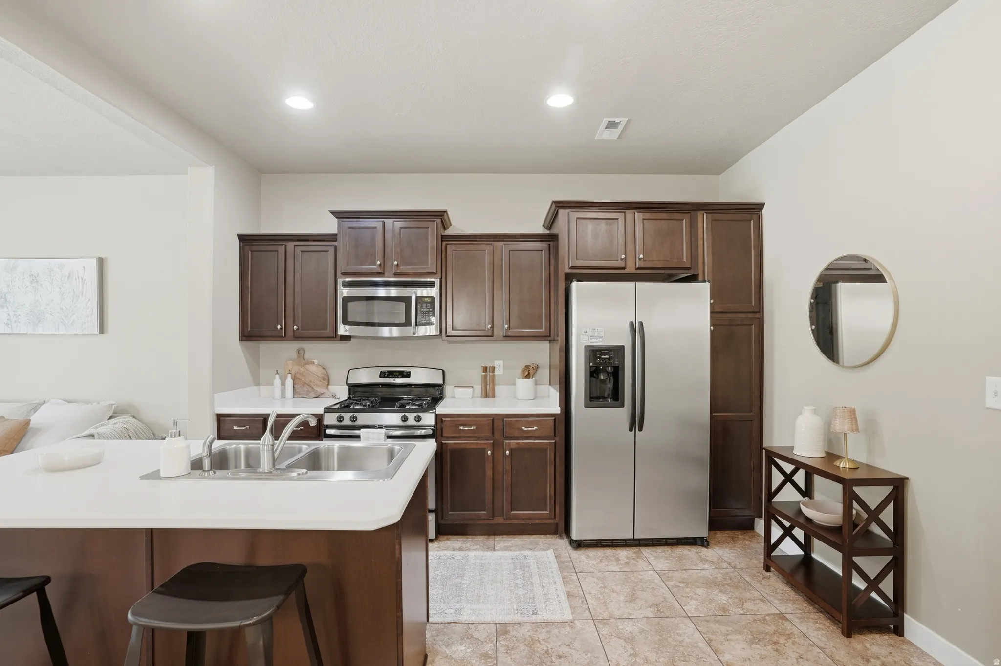 Kitchen featuring stainless steel appliances, dark wood finish cabinetry, light countertops, a breakfast bar, and recessed lighting