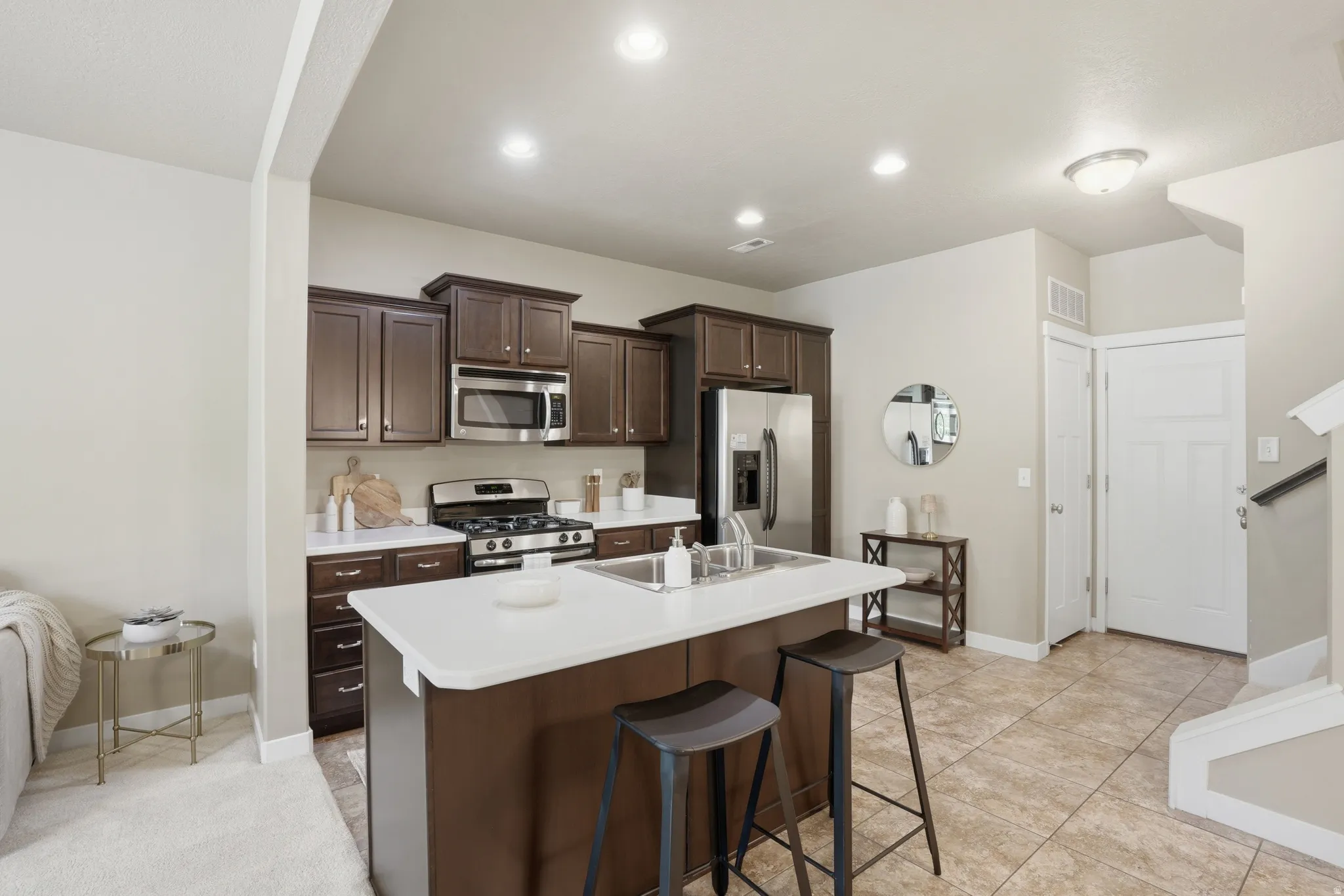 Kitchen featuring stainless steel appliances, a kitchen breakfast bar, dark wood finish cabinetry, a center island with sink, and light countertops