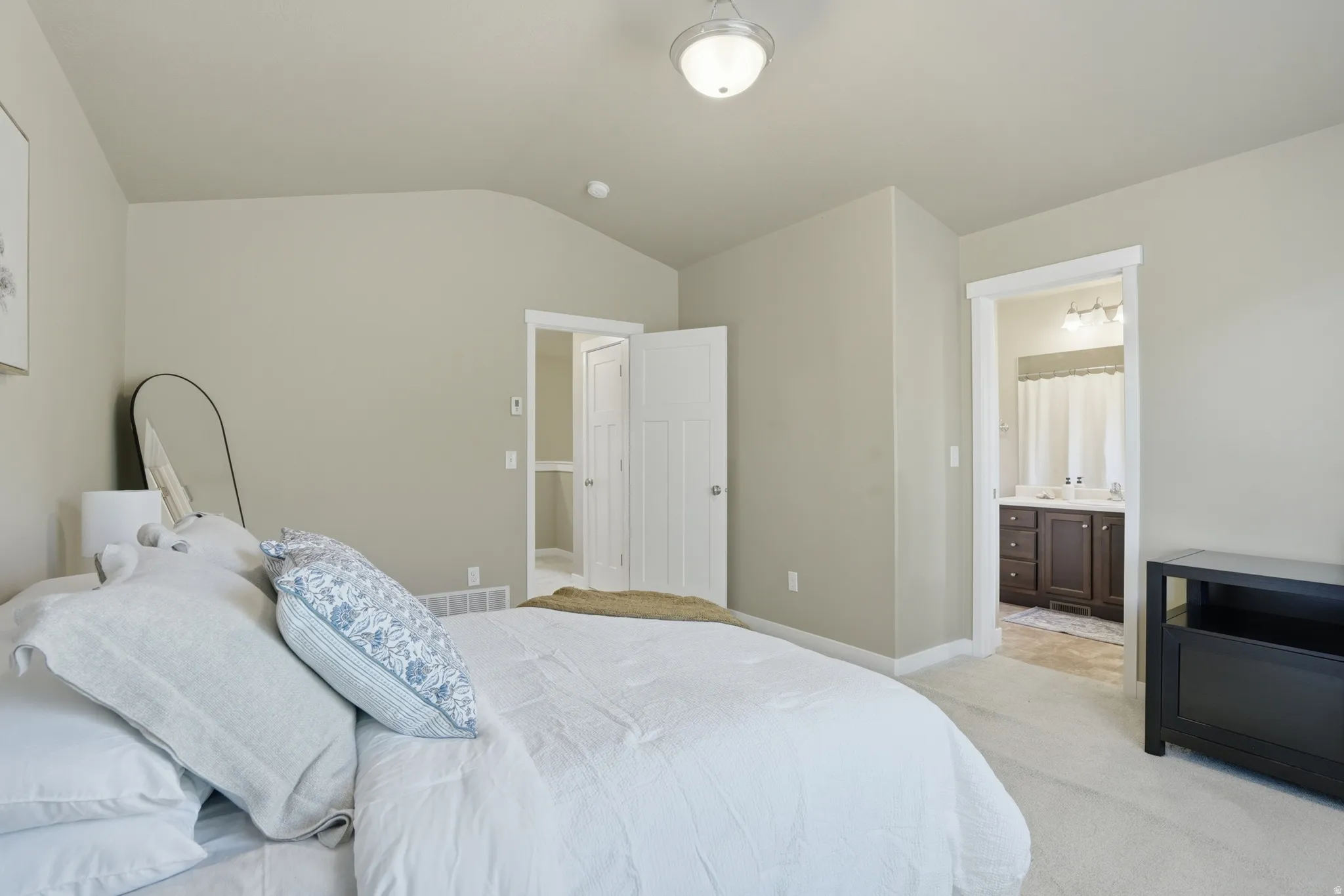 Bedroom featuring light carpet, lofted ceiling, and connected bathroom