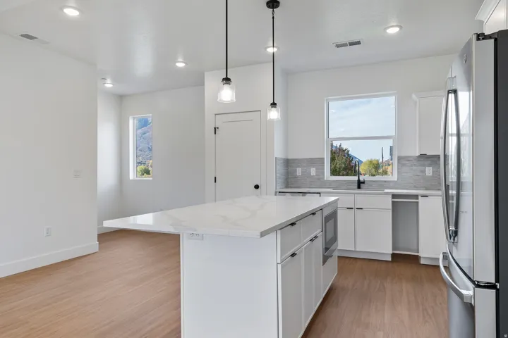 Kitchen with white cabinets, stainless steel appliances, light wood-style floors, light stone counters, and a kitchen island