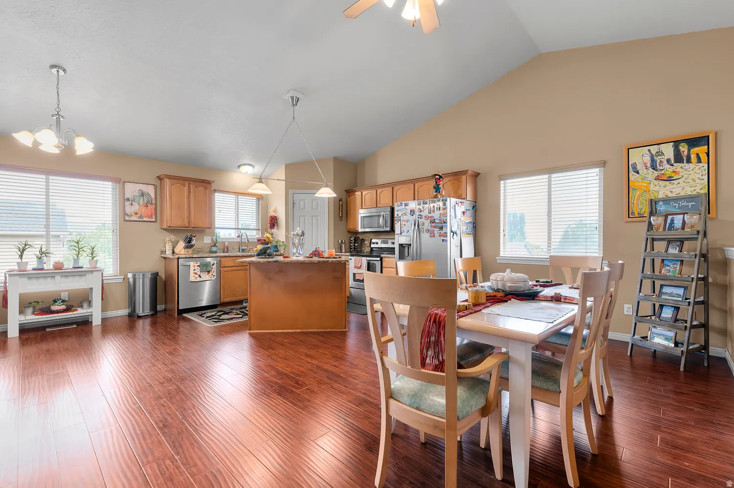 Dining area with ceiling fan, a chandelier, lofted ceiling, and dark wood-style flooring