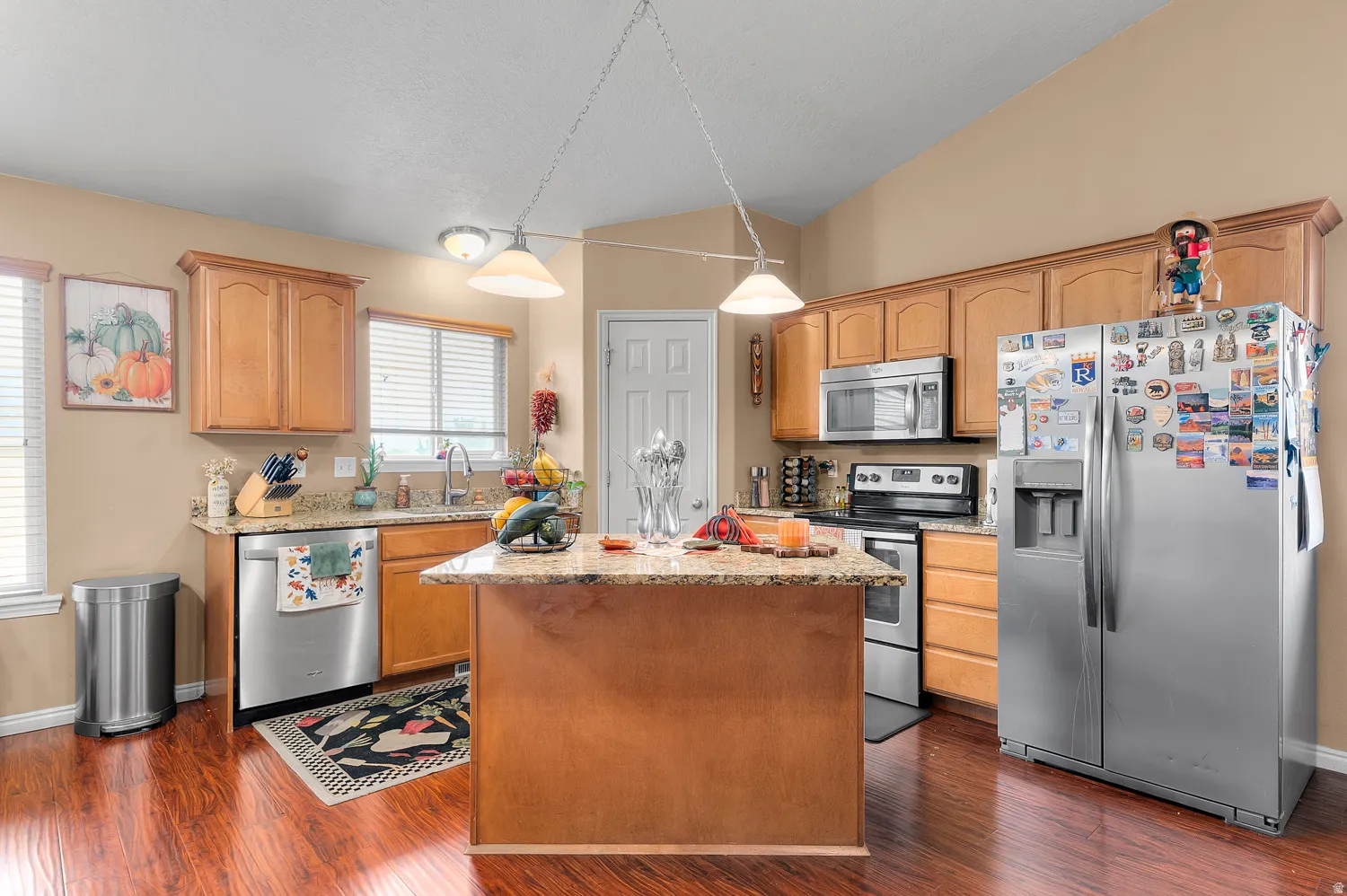 Kitchen featuring stainless steel appliances, light stone counters, pendant lighting, lofted ceiling, and a center island