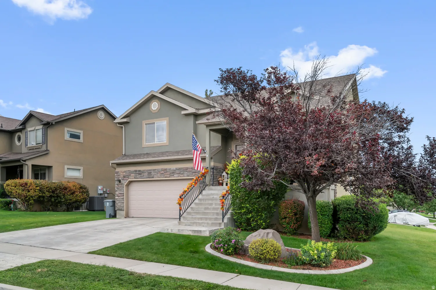 View of front of home with a garage, a front lawn, driveway, stucco siding, and stone siding