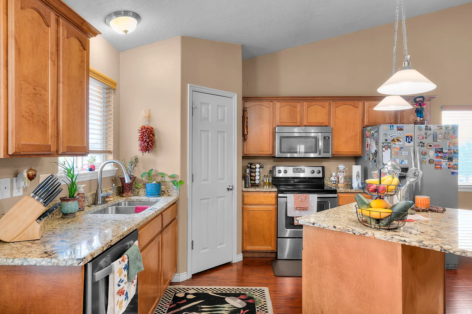 Kitchen with stainless steel appliances, light stone counters, hanging light fixtures, dark wood-type flooring, and vaulted ceiling
