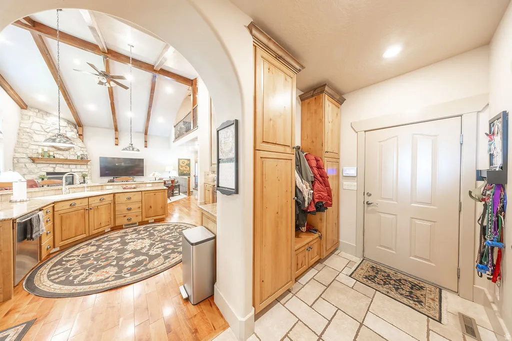 Kitchen featuring vaulted ceiling with beams, a ceiling fan, open floor plan, light stone counters, and light wood finish cabinets